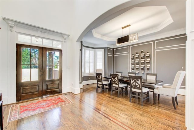 foyer entrance with arched walkways, french doors, a tray ceiling, crown molding, and a decorative wall