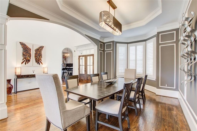 dining space with a tray ceiling, arched walkways, and wood finished floors