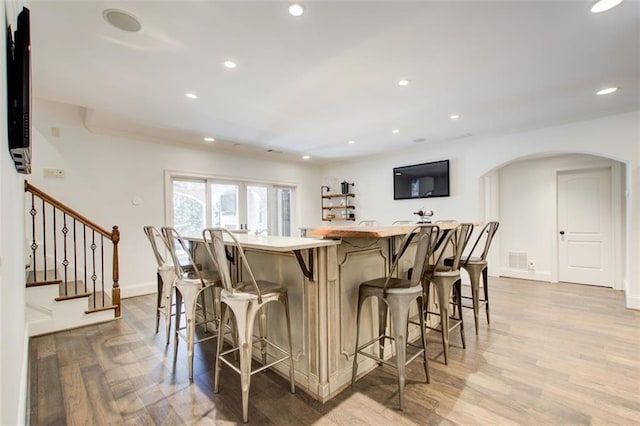 kitchen featuring arched walkways, visible vents, light countertops, light wood-style flooring, and a kitchen bar