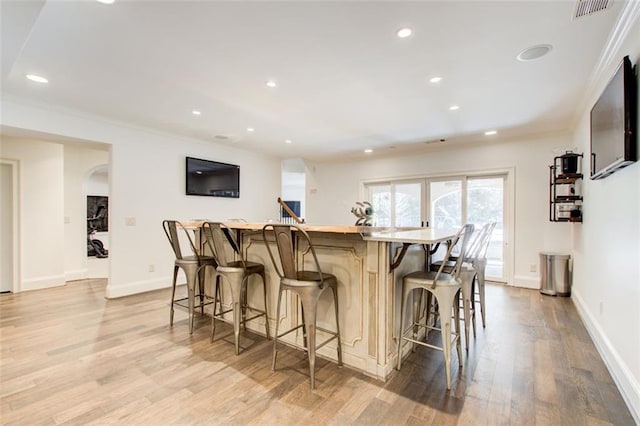 kitchen featuring crown molding, light wood finished floors, light countertops, a kitchen island, and a kitchen bar