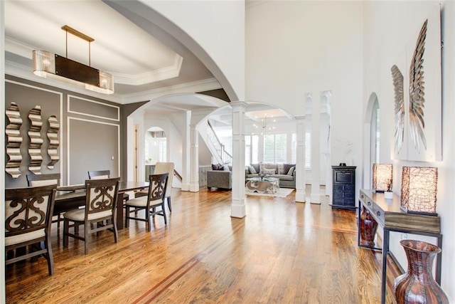 entrance foyer featuring decorative columns, arched walkways, a raised ceiling, wood finished floors, and crown molding