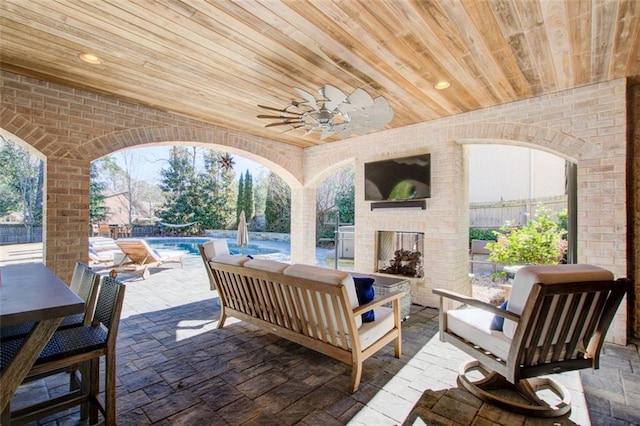 view of patio / terrace with an outdoor living space with a fireplace, fence, a ceiling fan, and an outdoor pool