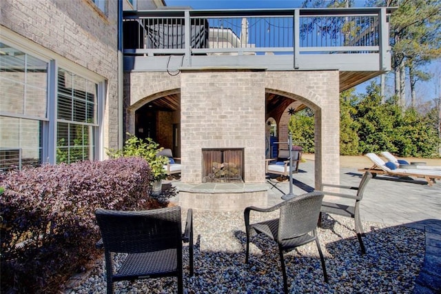 view of patio with an outdoor brick fireplace and a balcony