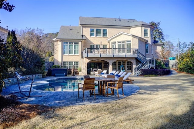 back of property featuring a patio, a balcony, stairs, stucco siding, and a hot tub