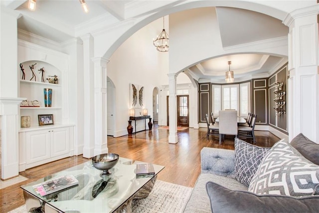 living area with built in shelves, arched walkways, decorative columns, ornamental molding, and wood finished floors