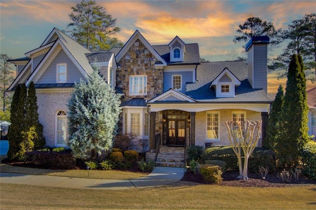 view of front of home with stone siding, a chimney, a standing seam roof, french doors, and a front lawn