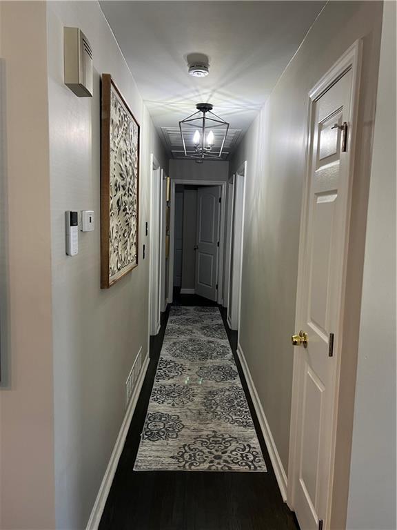 corridor featuring visible vents, baseboards, and dark wood-style flooring