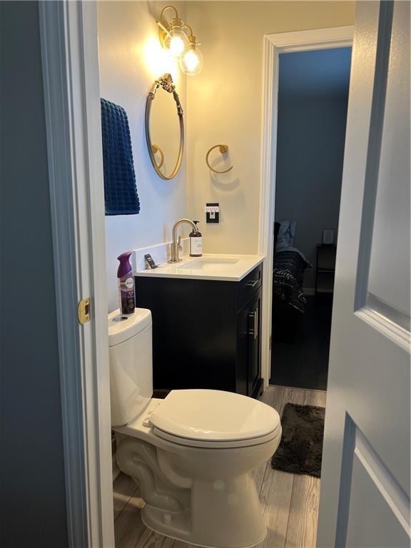 half bath with toilet, wood finished floors, and vanity