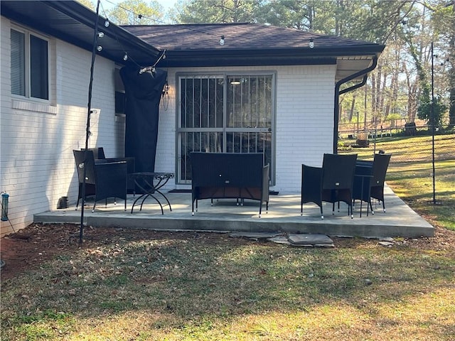 rear view of property featuring fence, a yard, roof with shingles, brick siding, and a patio area