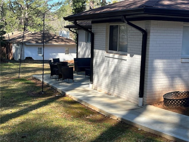 view of home's exterior with a yard, a patio area, brick siding, and a shingled roof