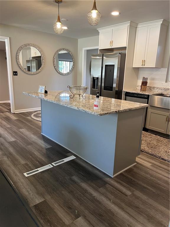 kitchen with light stone countertops, appliances with stainless steel finishes, dark wood finished floors, and a center island