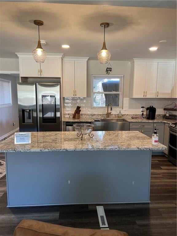 kitchen featuring a sink, a center island, light stone counters, stainless steel fridge, and dark wood-style flooring