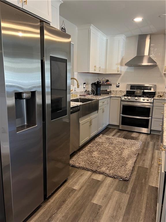 kitchen with dark wood finished floors, decorative backsplash, stainless steel appliances, wall chimney exhaust hood, and a sink