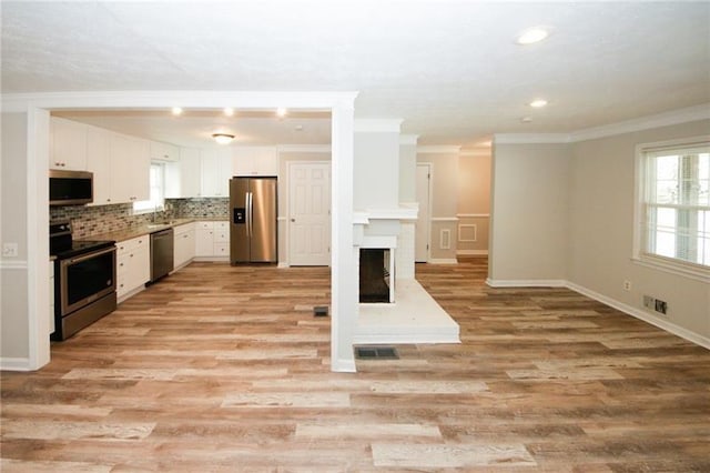 kitchen featuring white cabinetry, crown molding, light wood-type flooring, appliances with stainless steel finishes, and decorative backsplash