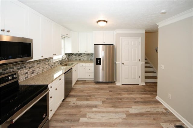 kitchen with stainless steel appliances, white cabinets, decorative backsplash, light wood-type flooring, and ornamental molding