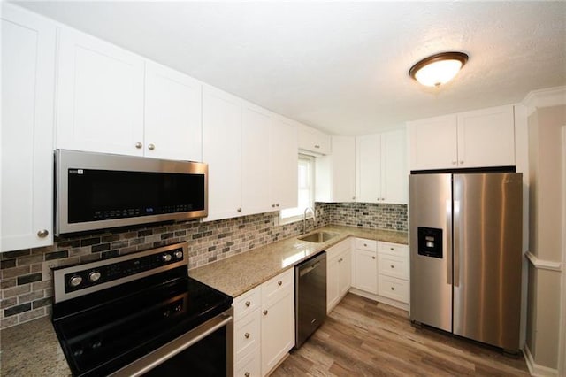 kitchen featuring appliances with stainless steel finishes, tasteful backsplash, sink, white cabinetry, and wood-type flooring