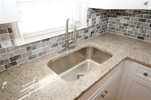 room details featuring sink, white cabinets, decorative backsplash, and light stone countertops