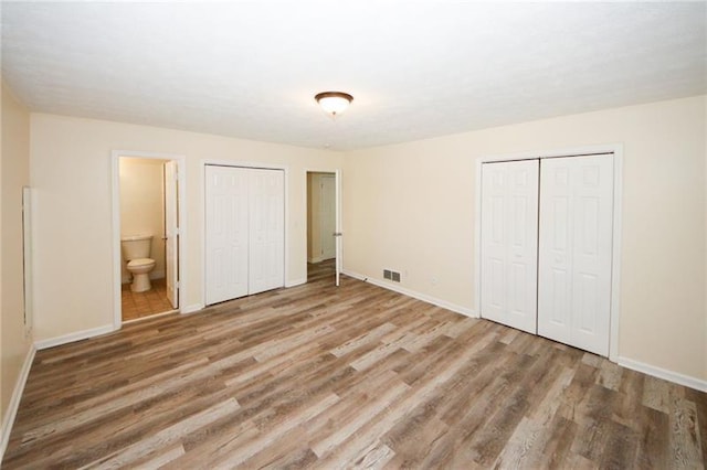 unfurnished bedroom with multiple closets, wood-type flooring, and ensuite bath