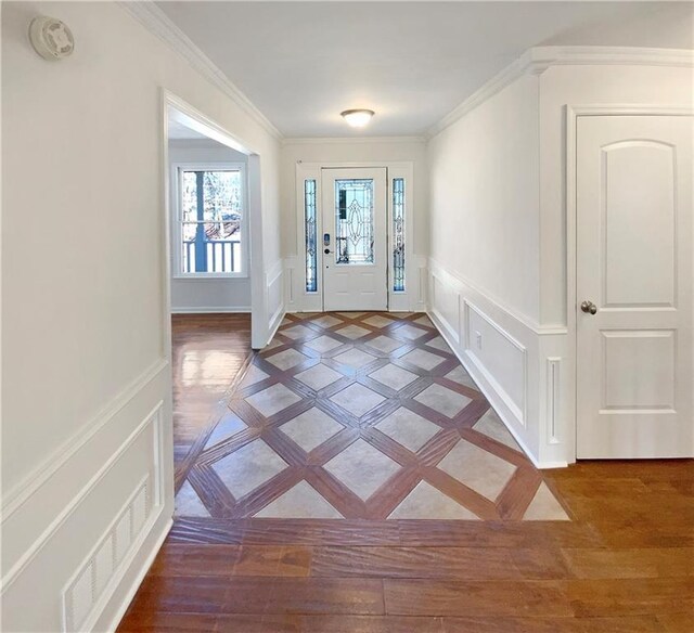 foyer featuring visible vents, crown molding, a wainscoted wall, light wood-style flooring, and a decorative wall