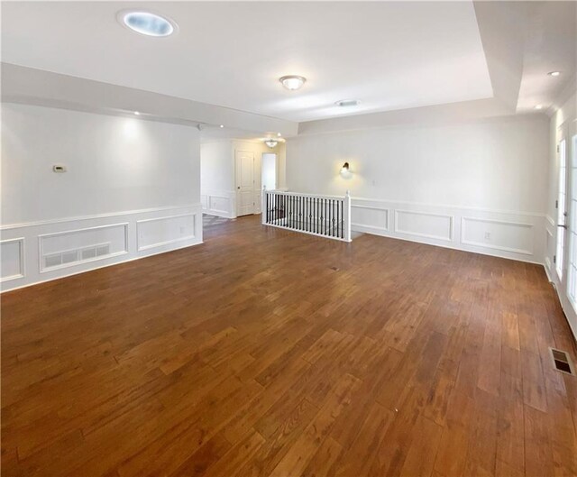 unfurnished room featuring visible vents, dark wood-style floors, and a decorative wall