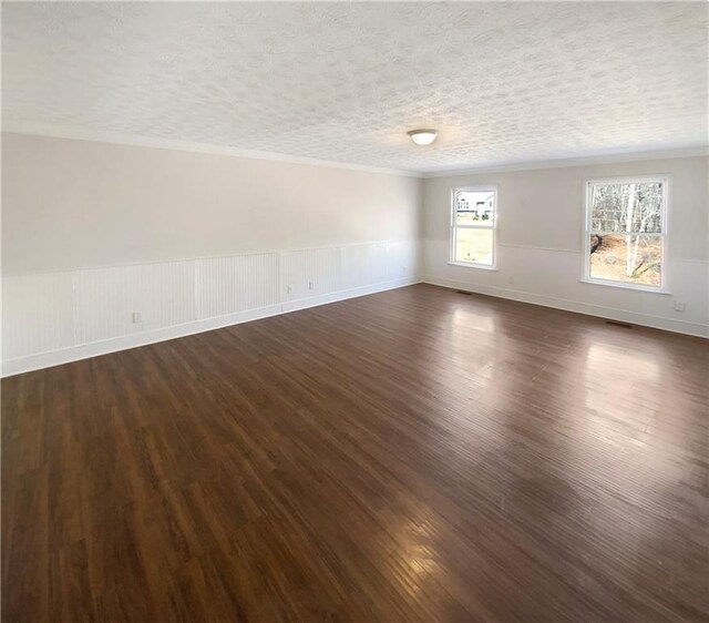 empty room with a wainscoted wall, a textured ceiling, dark wood-style floors, and ornamental molding