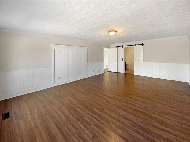 unfurnished room with dark wood-style floors, a wainscoted wall, visible vents, a textured ceiling, and a barn door