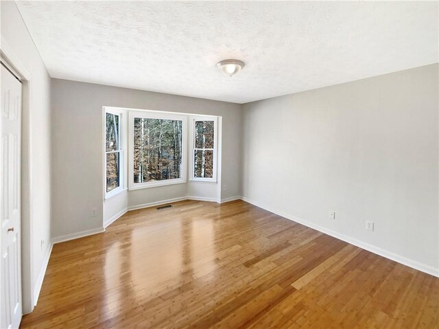 spare room with baseboards, visible vents, light wood finished floors, and a textured ceiling