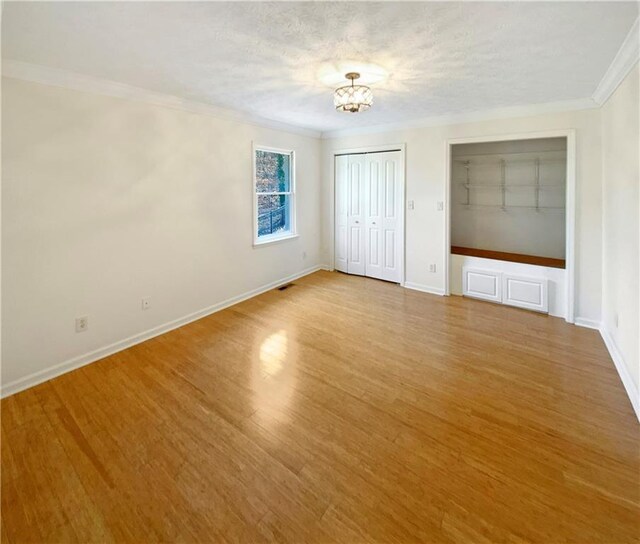 unfurnished bedroom with crown molding, baseboards, light wood-style flooring, a notable chandelier, and a textured ceiling