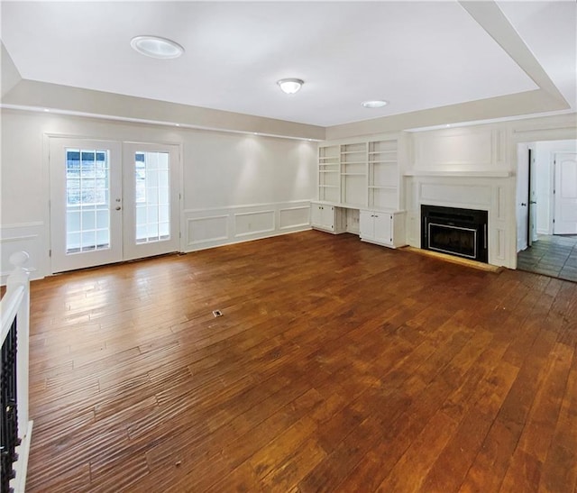 unfurnished living room with dark wood finished floors, french doors, a decorative wall, wainscoting, and a fireplace