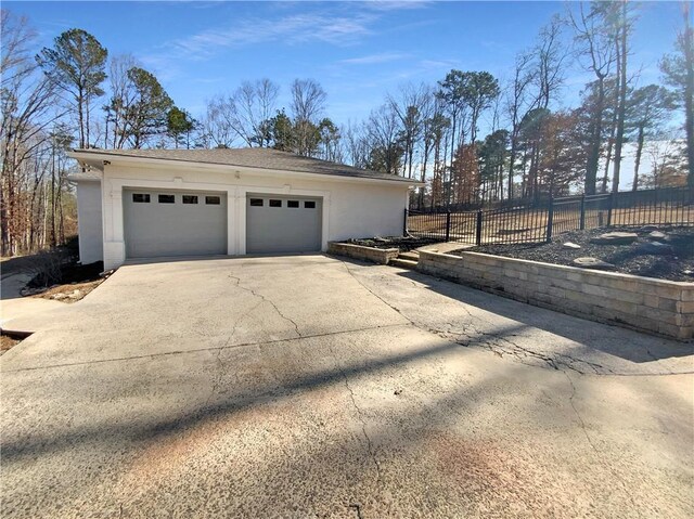 garage featuring concrete driveway and fence