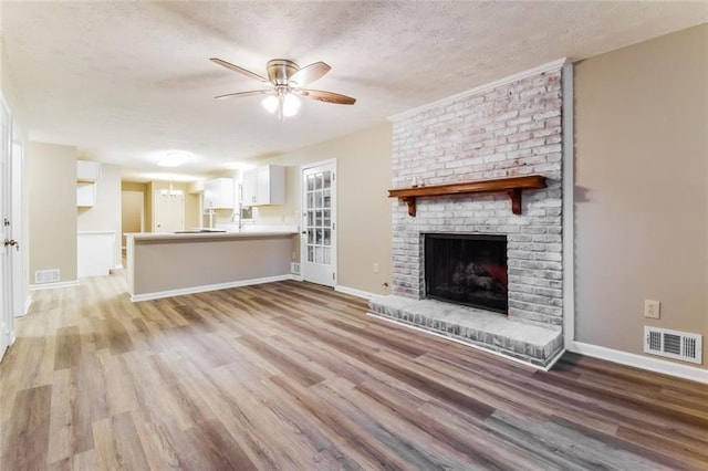 unfurnished living room with ceiling fan, light hardwood / wood-style flooring, a fireplace, and a textured ceiling