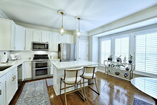 kitchen featuring stainless steel appliances, white cabinets, hanging light fixtures, light countertops, and a center island