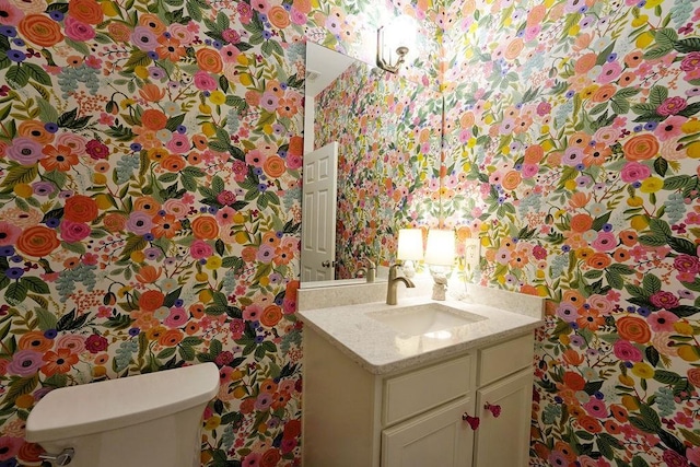 half bath with toilet, vanity, and wallpapered walls