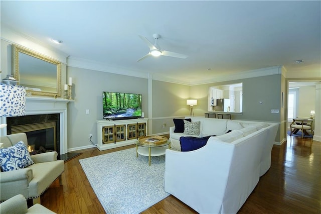 living room with a fireplace, crown molding, ceiling fan, and dark wood-type flooring