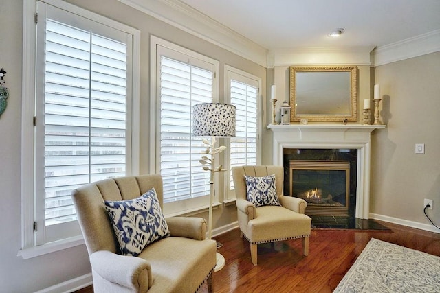 sitting room featuring a glass covered fireplace, crown molding, baseboards, and wood finished floors