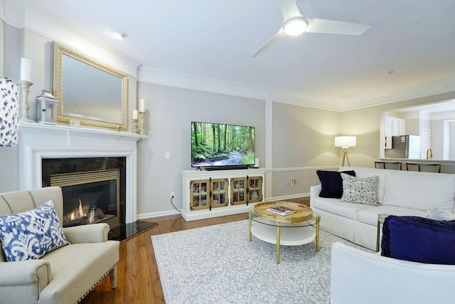 living area featuring crown molding, ceiling fan, wood finished floors, and a high end fireplace