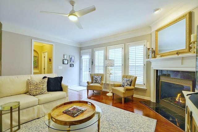 living room featuring crown molding, a premium fireplace, ceiling fan, wood finished floors, and baseboards