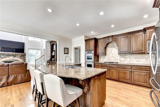 kitchen featuring crown molding, light stone counters, a sink, premium range hood, and stainless steel appliances