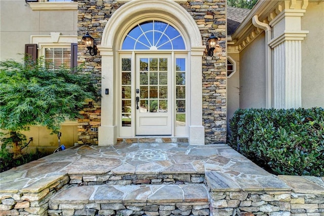 property entrance featuring a shingled roof, stone siding, and stucco siding