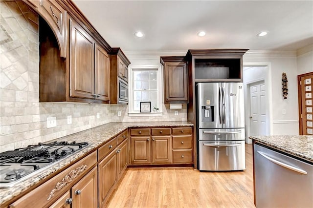 kitchen with light wood-style floors, appliances with stainless steel finishes, ornamental molding, and light stone counters