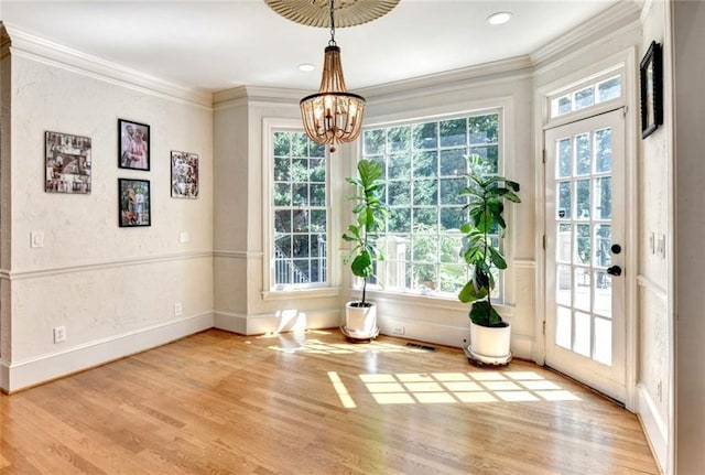 doorway with visible vents, ornamental molding, wood finished floors, baseboards, and a notable chandelier