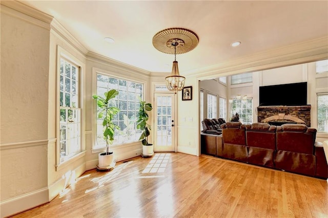 interior space featuring an inviting chandelier, light wood-style floors, a stone fireplace, baseboards, and ornamental molding
