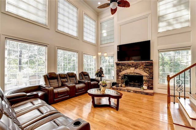 living room with a towering ceiling, a stone fireplace, stairway, a ceiling fan, and a wealth of natural light