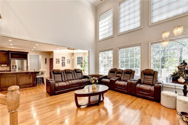 living room featuring ornamental molding, light wood-style flooring, and a towering ceiling