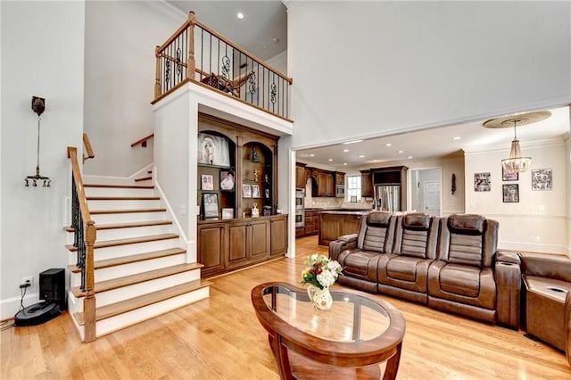 living room with crown molding, stairs, a towering ceiling, recessed lighting, and light wood finished floors