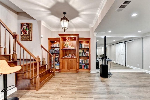 entryway with visible vents, light wood-type flooring, a barn door, ornamental molding, and stairs