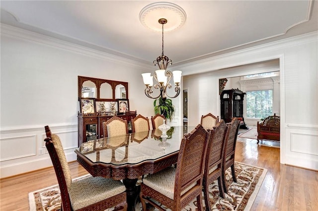 dining area featuring light wood-style floors, ornamental molding, wainscoting, and a chandelier