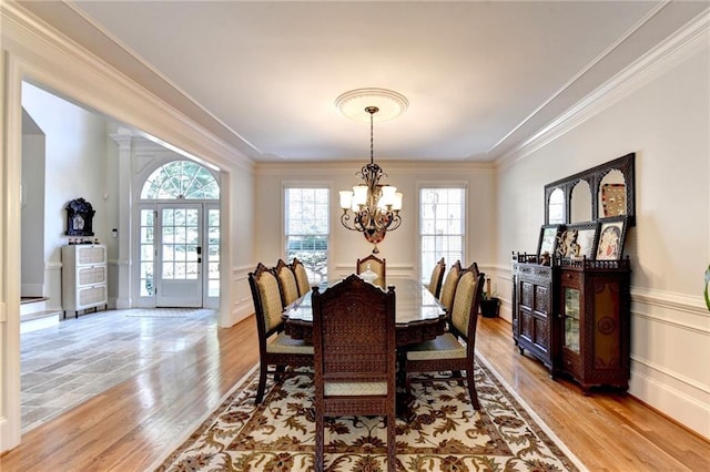 dining area featuring crown molding, a decorative wall, a chandelier, and light wood-style floors