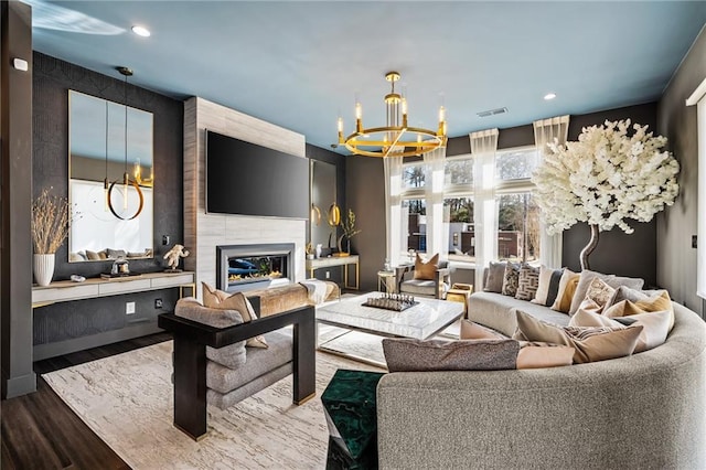 living room featuring an inviting chandelier, a large fireplace, and wood-type flooring