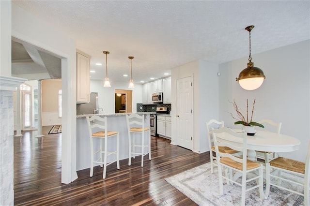 kitchen featuring white cabinets, kitchen peninsula, stainless steel appliances, and tasteful backsplash